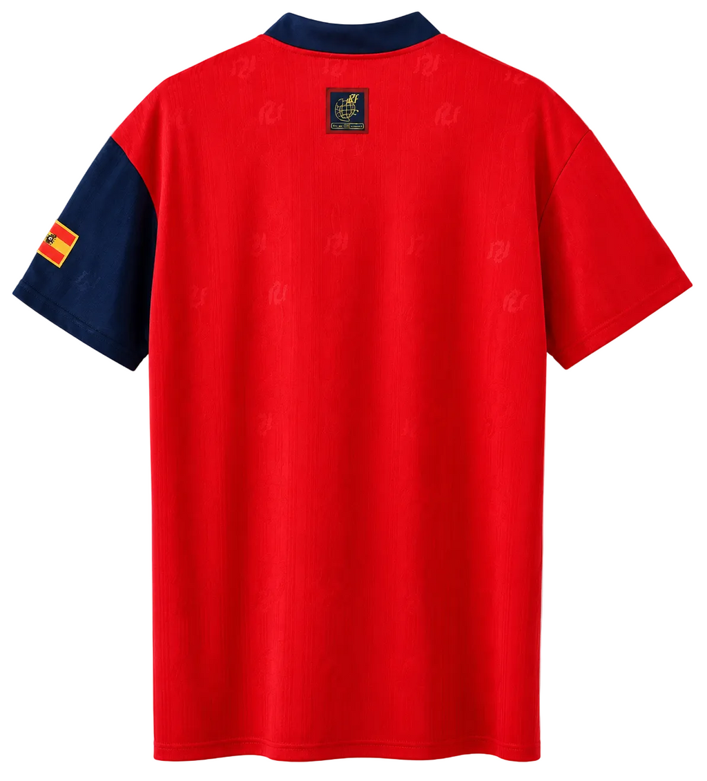A red short-sleeve soccer jersey shown from the back, featuring a navy blue collar and sleeve, a small Spanish flag patch on the sleeve, and a crest patch at the back neck.